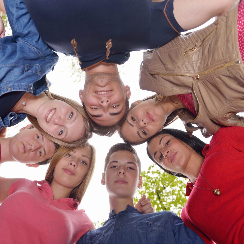 Happy smiling group of young friends staying together outdoor in the park